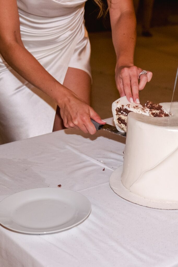 Gros plan sur la mariée découpant le gâteau de mariage lors de la réception au Château Fengari, près de Bordeaux, robe blanche élégante et détail de la pièce montée capturé par un photographe de mariage.