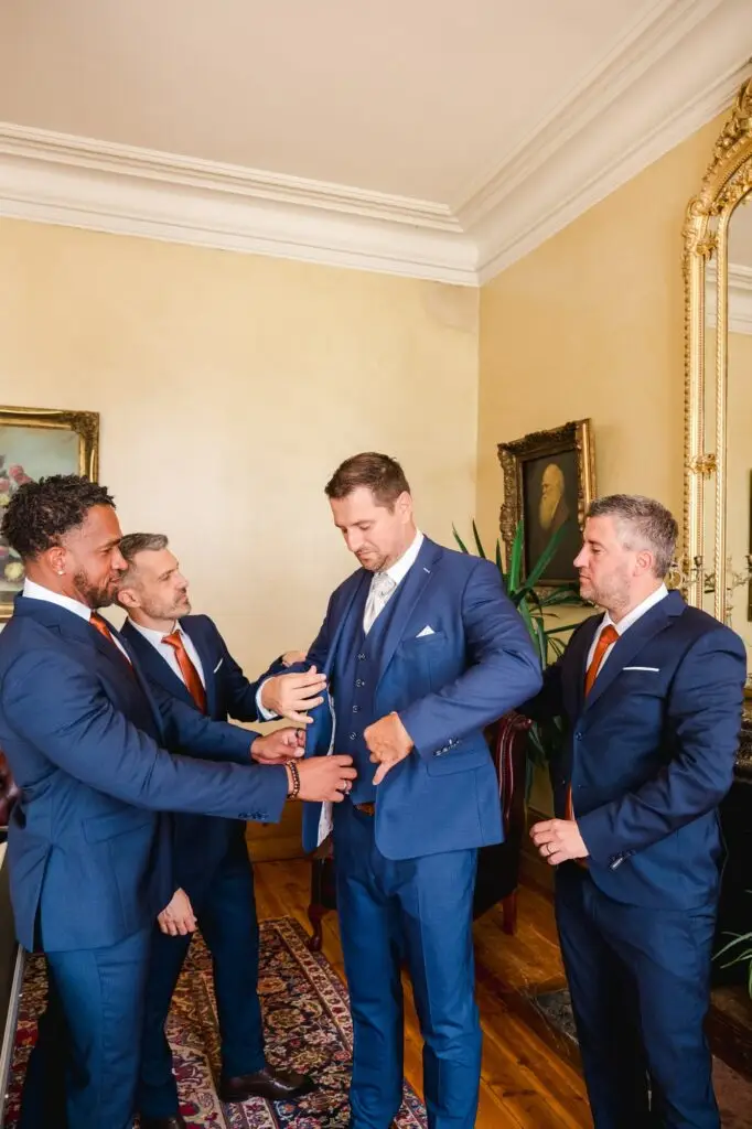 Photographie de mariage au Château Fengari près de Bordeaux, montrant les témoins aidant le marié à se préparer.