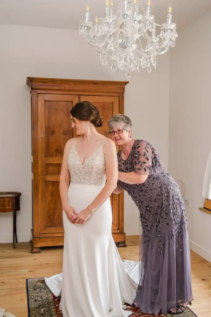 Détail des mains aidant la mariée à fermer sa robe pendant les préparatifs au Château Gassies à Bordeaux.