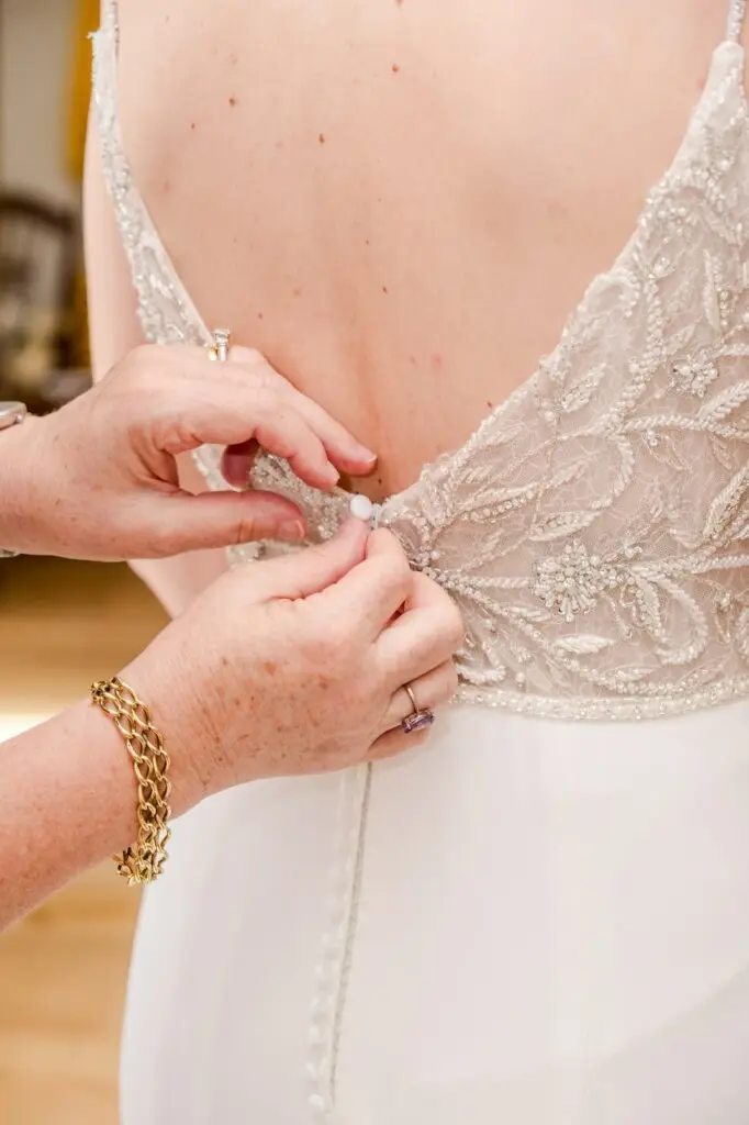 Détail des mains aidant la mariée à fermer sa robe pendant les préparatifs au Château Gassies à Bordeaux.