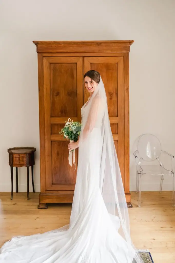 Portrait de la mariée en robe et voile devant une armoire ancienne au Château Gassies à Bordeaux.