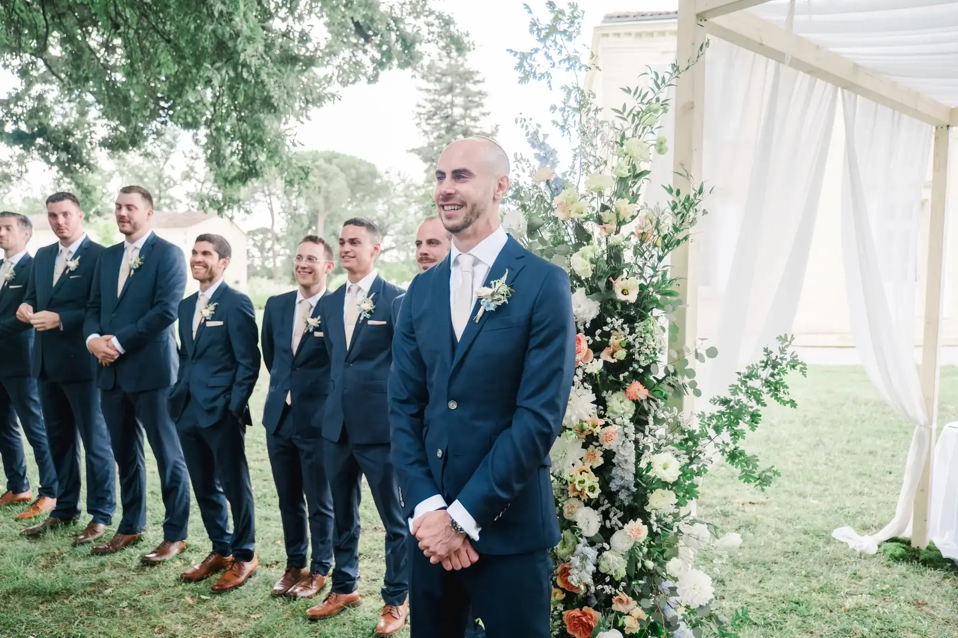 Marié attendant la mariée sous l’arche fleurie lors de la cérémonie au Château Gassies à Bordeaux.