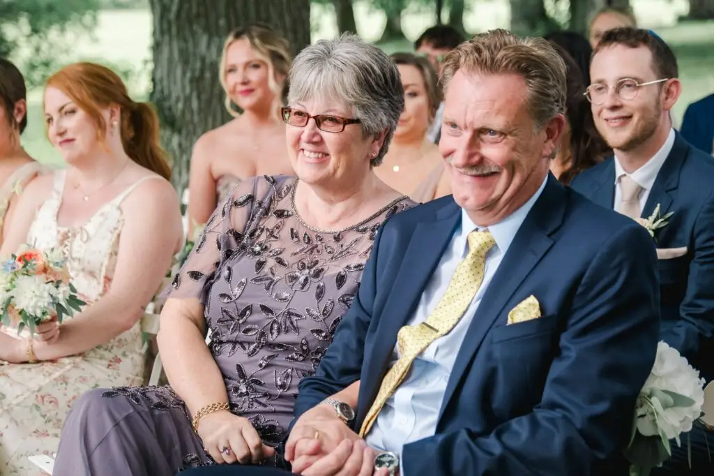 Parents des mariés souriant pendant la cérémonie de mariage en extérieur au Château Gassies à Bordeaux.