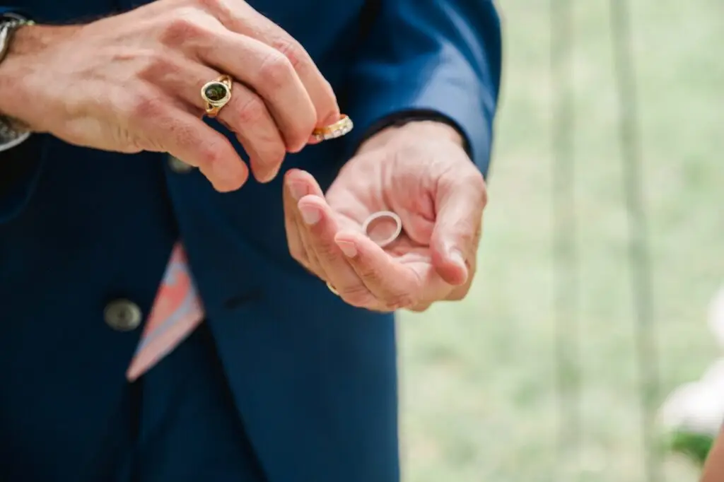 Gros plan sur les mains des mariés au moment de l’échange des alliances pendant la cérémonie de mariage en extérieur