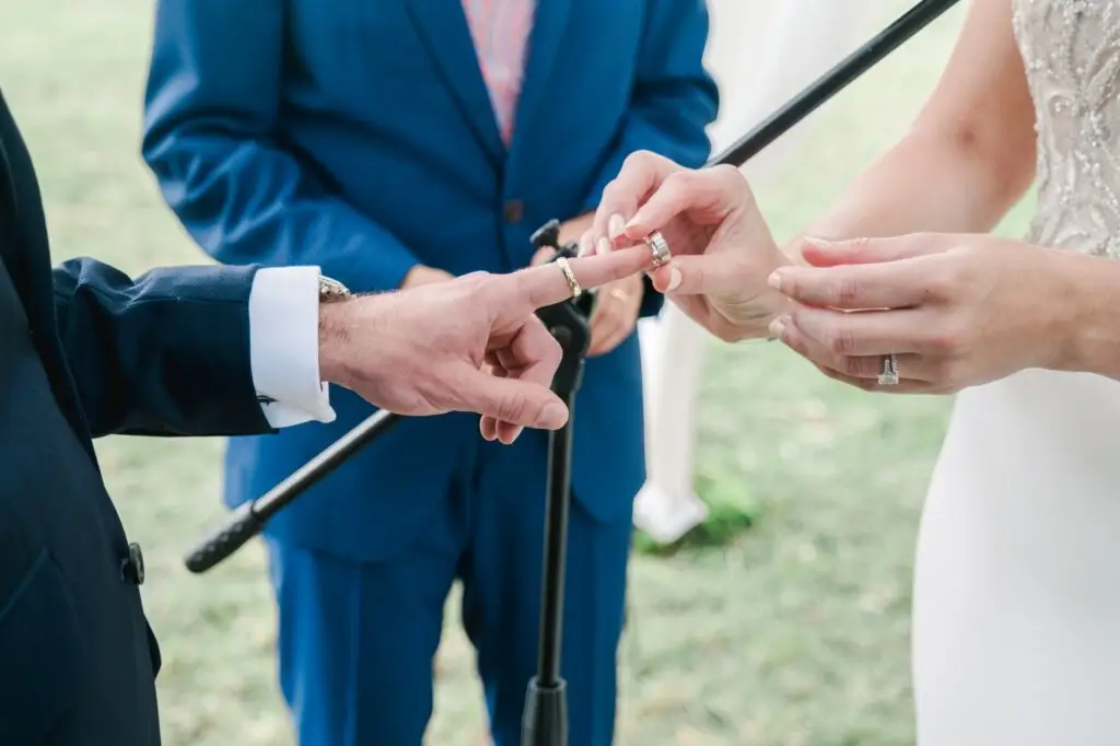 La mariée passe l’alliance au doigt du marié pendant la cérémonie, sous l’arche fleurie