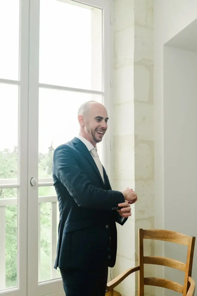 Marié en costume souriant pendant les préparatifs de mariage au Château Gassies près de Bordeaux, lumière naturelle.