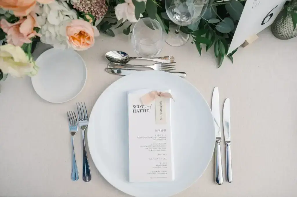 Vue de dessus d’une assiette avec menu de mariage personnalisé, couverts et décoration florale