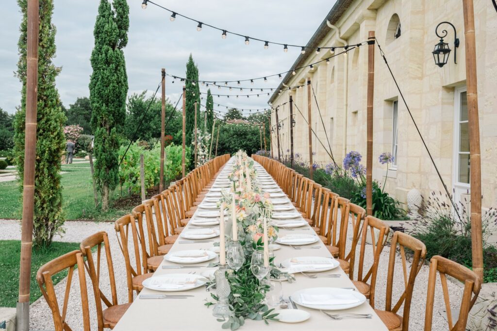 Longue table de réception de mariage dressée en extérieur au Château Gassies près de Bordeaux, avec guirlandes lumineuses et décoration florale