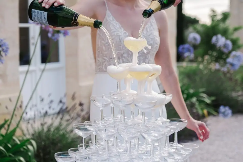 Gros plan sur le champagne coulant dans une pyramide de coupes lors d’un mariage au Château Gassies