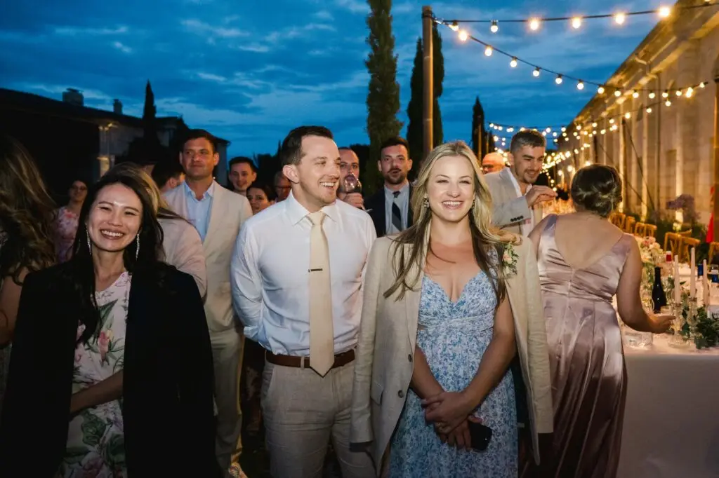 Les invités sourient et profitent de la soirée de mariage sous les guirlandes lumineuses au château Gassies