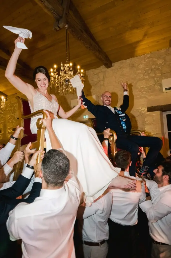 La mariée et le marié sont portés sur des chaises par leurs invités lors d’un moment festif sur la piste de danse.