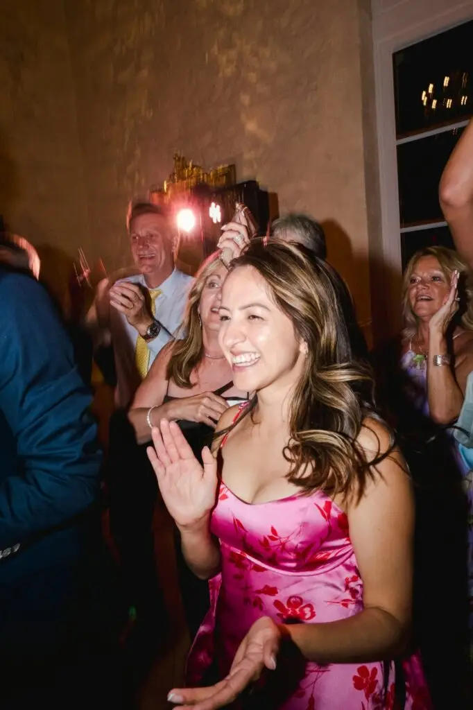 Une invitée sourit et applaudit pendant la soirée dansante du mariage, éclairée par les lumières de la piste.