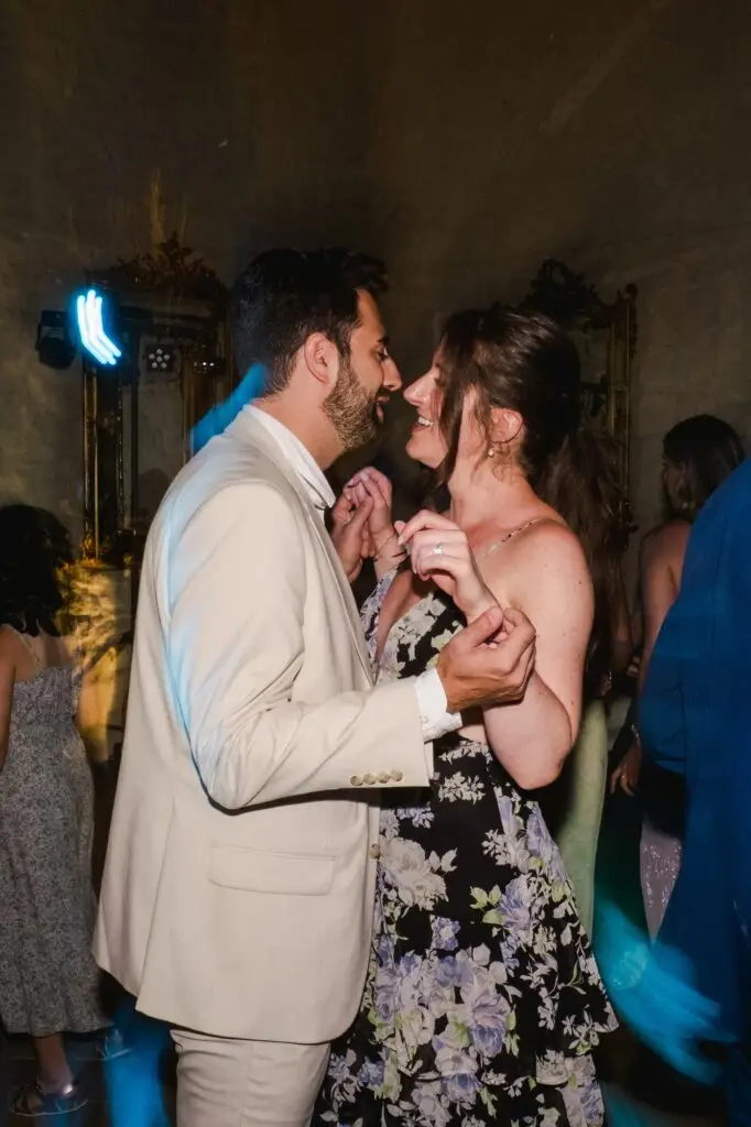 Un couple d’invités se regarde en souriant tout en dansant sous les lumières colorées de la soirée.