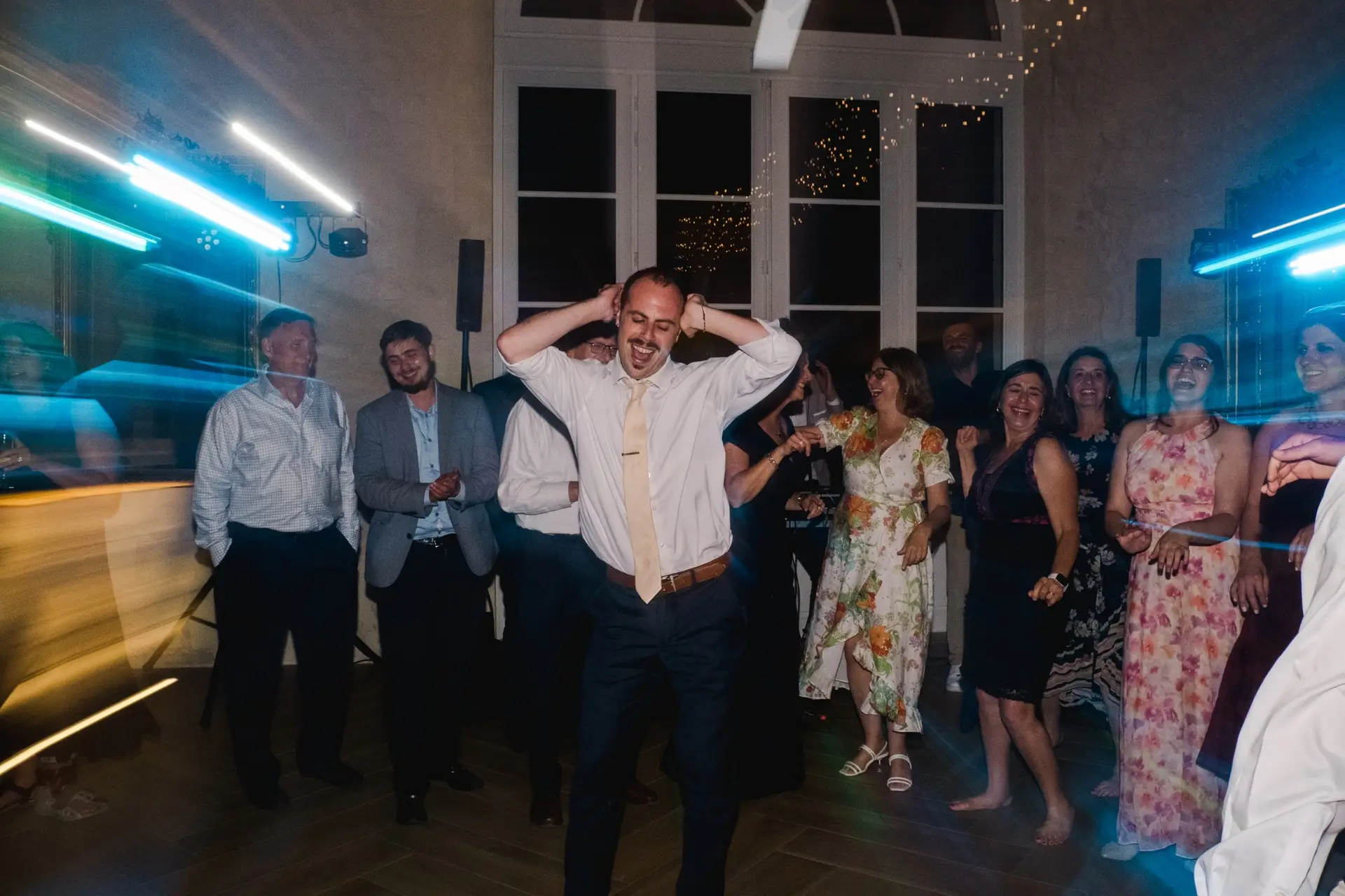 Invité dansant avec énergie au milieu des convives lors de la soirée de mariage, entouré de lumières colorées et d’une ambiance festive.