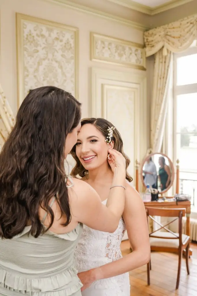 Une proche aide la mariée à ajuster ses boucles d’oreilles pendant les préparatifs dans une chambre du Château Pape Clément, photo Julien Boyer