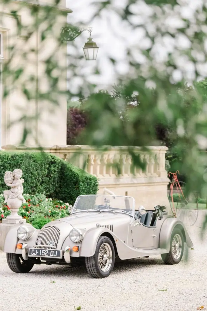 Voiture de mariage ancienne stationnée dans les jardins du Château Pape Clément à Pessac, reportage photo de mariage par Julien Boyer