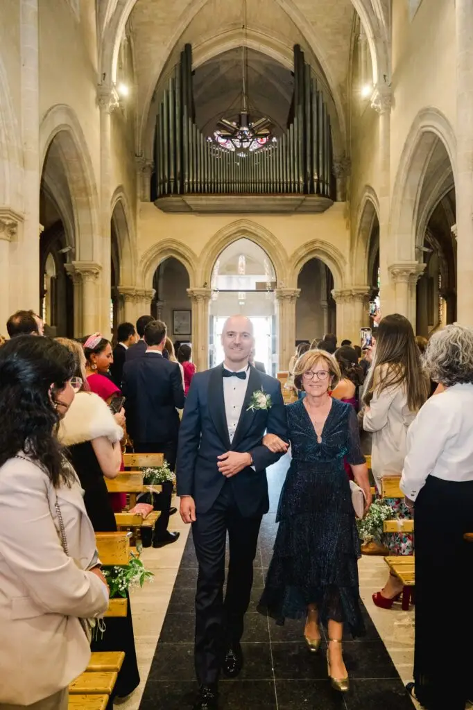 Le marié fait son entrée dans l’église de Caudéran à Bordeaux au bras d’une proche lors de la cérémonie de mariage, photo par Julien Boyer photographe de mariage