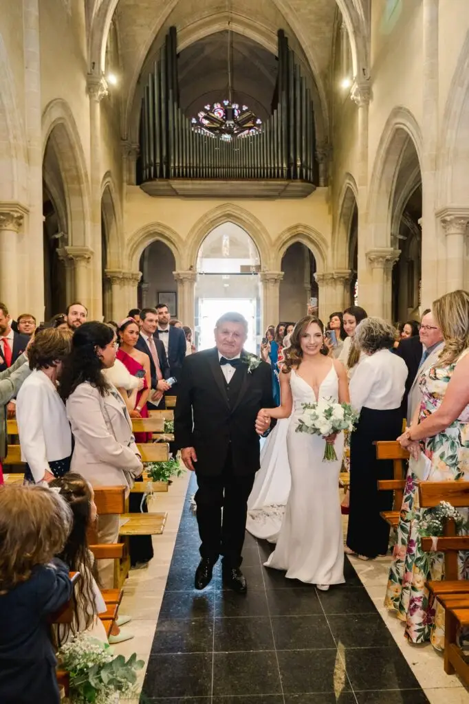 La mariée fait son entrée dans l’église de Caudéran à Bordeaux au bras de son père, entourée des invités lors de la cérémonie de mariage, photo par Julien Boyer