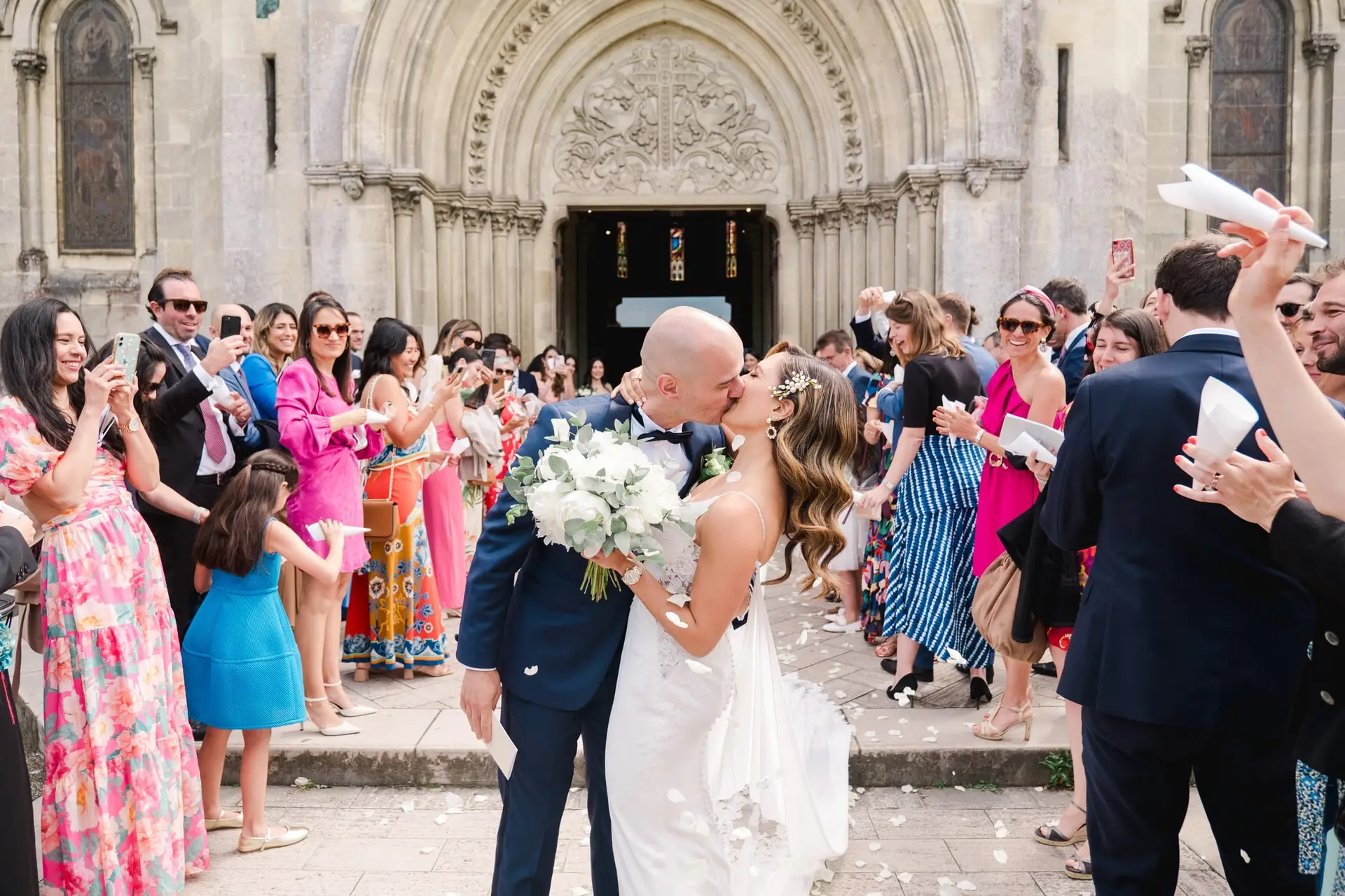 Les mariés s’embrassent à la sortie de l’église de Caudéran à Bordeaux sous les pétales et les applaudissements des invités, photo par Julien Boyer photographe de mariage