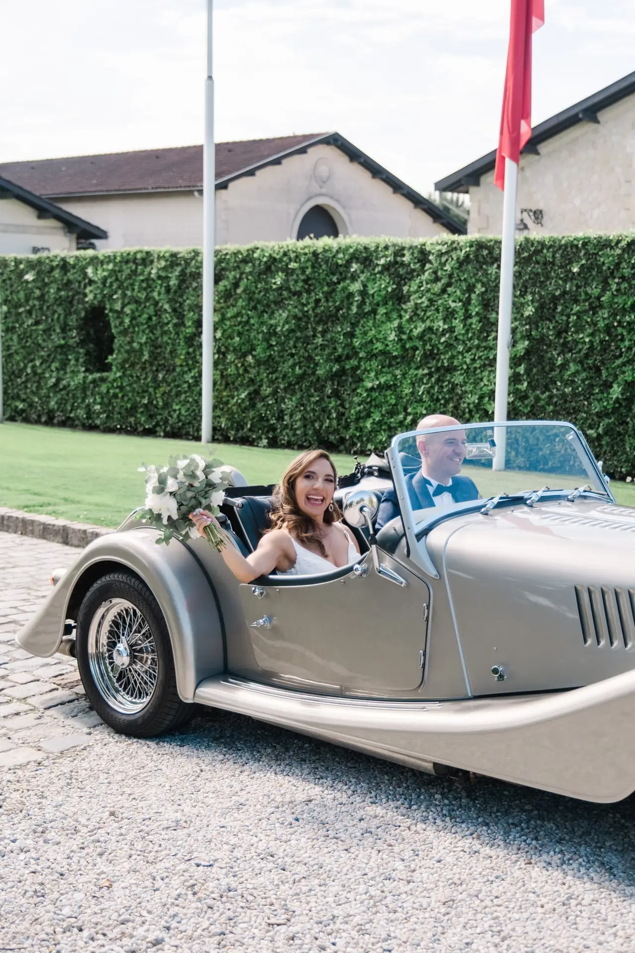 La mariée souriante arrive en voiture de collection avec le marié au Château Pape Clément à Pessac, reportage photo de mariage par Julien Boyer