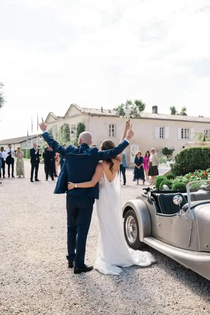 Les mariés lèvent les bras et saluent leurs invités dans la cour du Château Pape Clément à Pessac, ambiance joyeuse capturée par Julien Boyer
