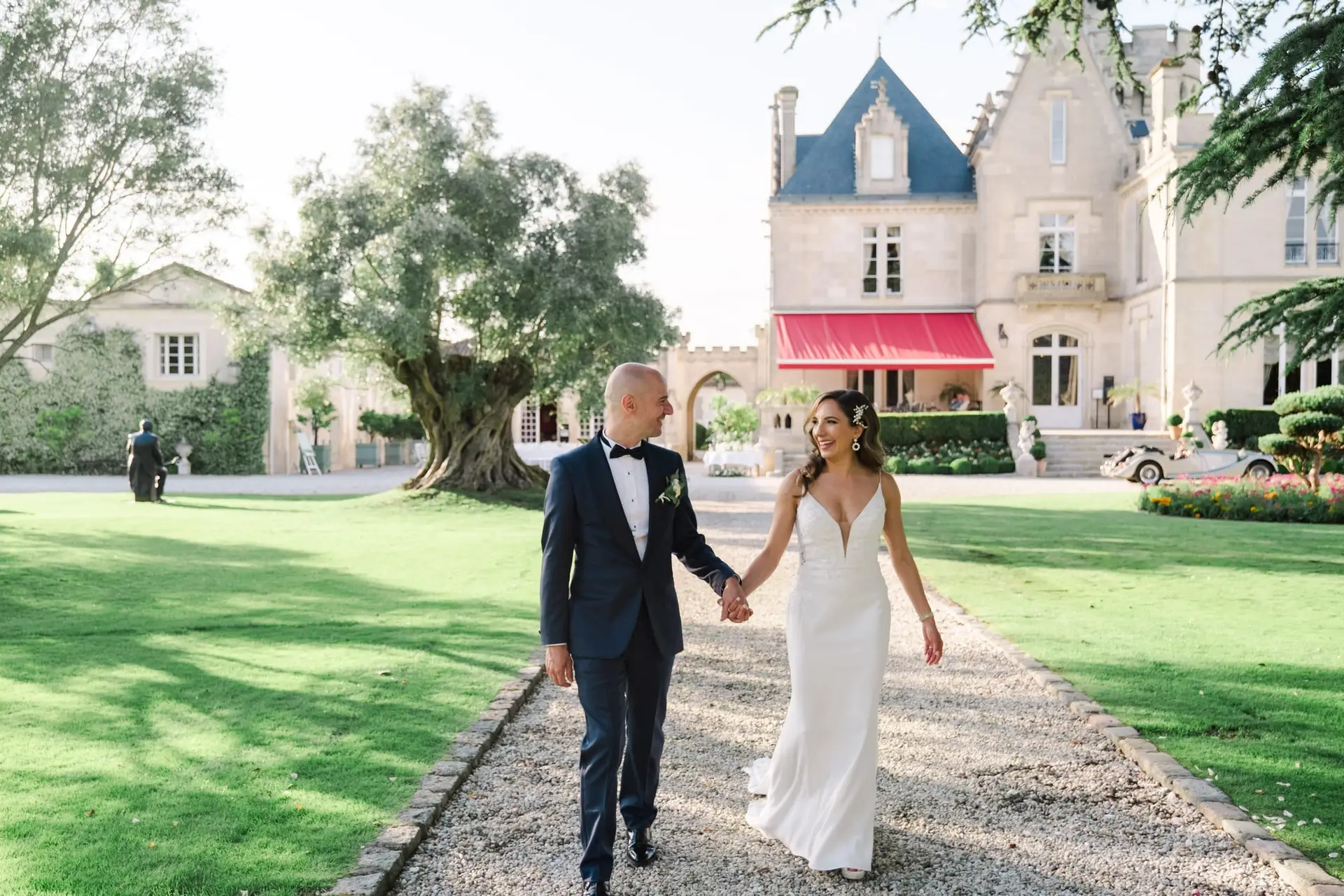 Les mariés marchent main dans la main devant le Château Pape Clément à Pessac lors de leur séance photo de mariage, photo par Julien Boyer