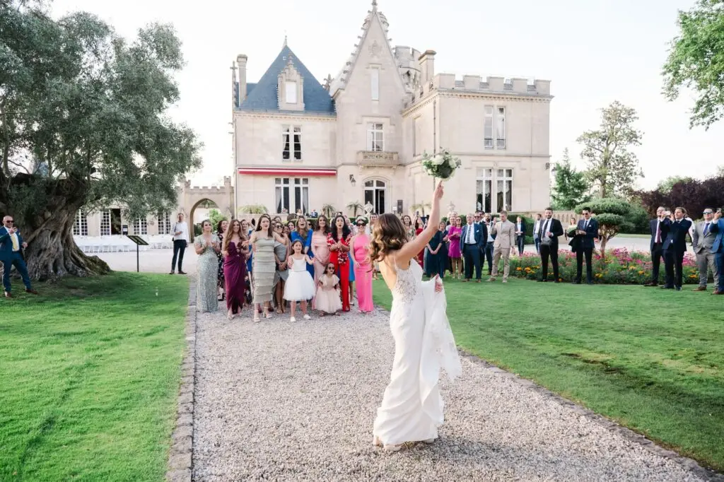 La mariée lance son bouquet devant le Château Pape Clément à Pessac, entourée de ses invitées lors du mariage, photo par Julien Boyer