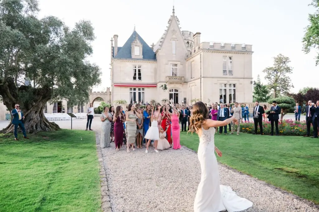 Invitées réagissant avec enthousiasme lors du lancer du bouquet dans les jardins du Château Pape Clément à Pessac, photo de mariage par Julien Boyer