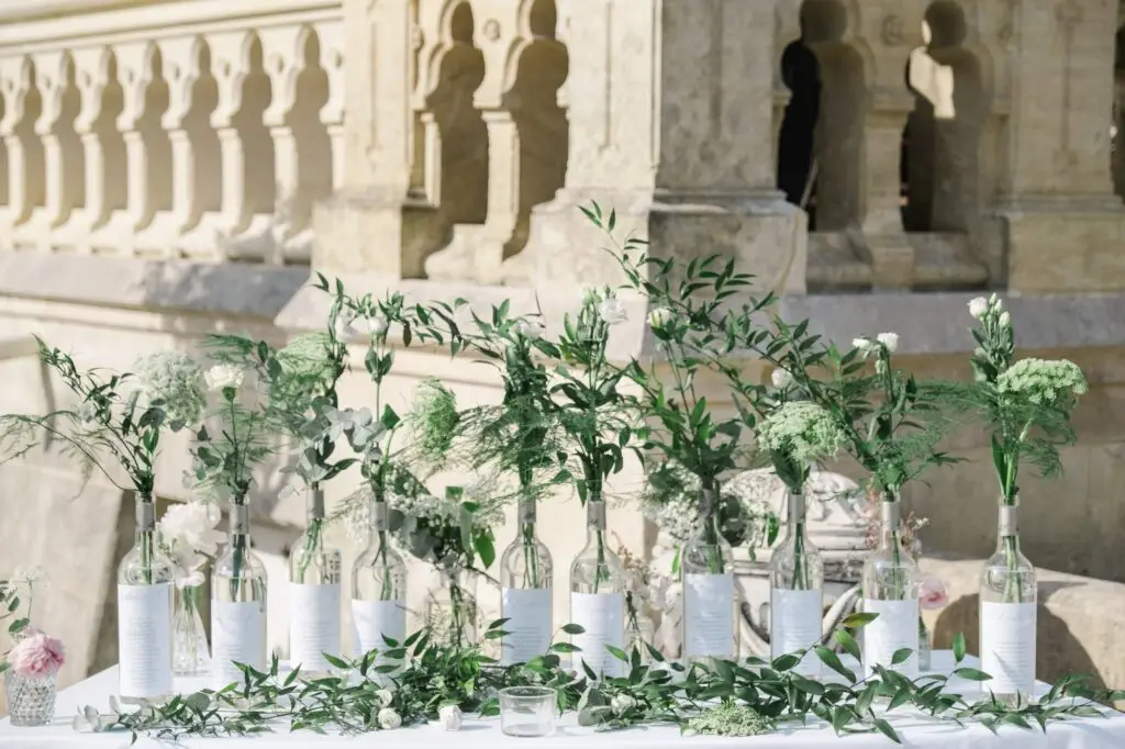 Plan de table de mariage avec bouteilles décorées de fleurs et papeterie élégante au Château Pape Clément à Pessac, photographie de Julien Boyer