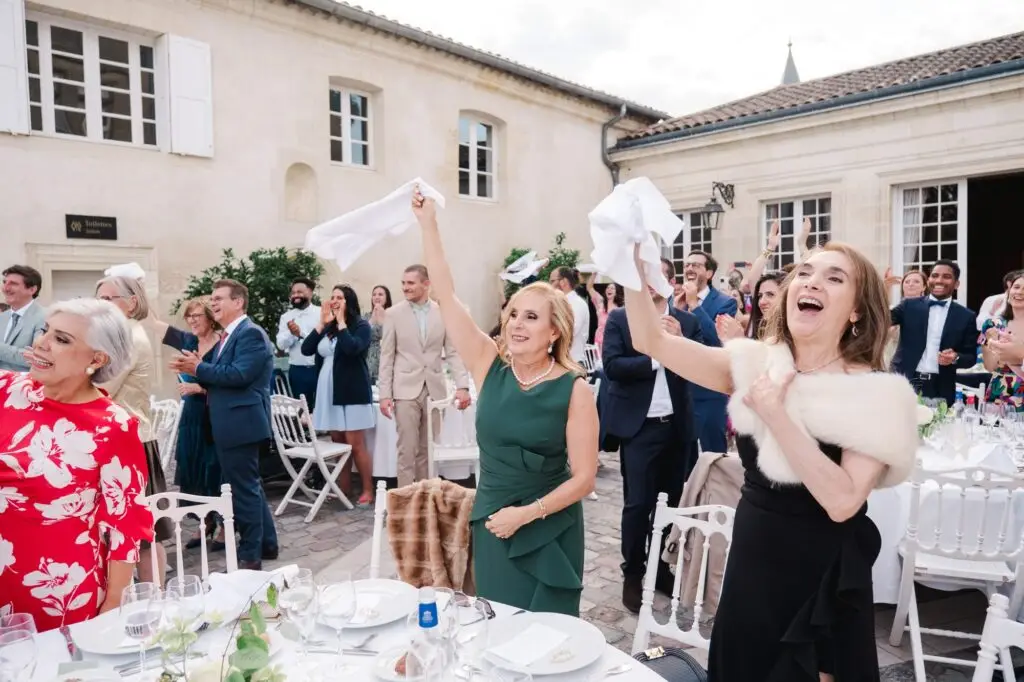 Invités applaudissant et agitant leurs serviettes pendant le dîner de mariage au Château Pape Clément à Pessac, photo par Julien Boyer