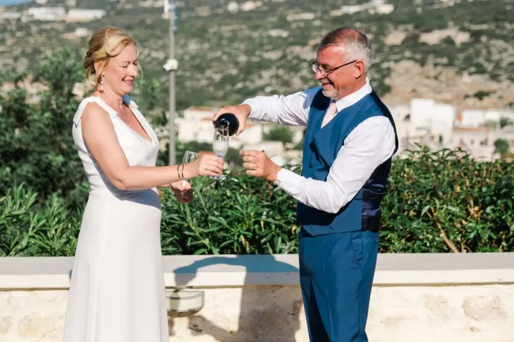 Marié servant le champagne à la mariée lors de leur mariage à Rethymnon en Crète, moment de célébration capturé par Julien Boyer