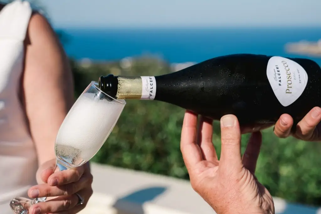 Service du champagne lors d’un mariage à Agreco Farm près de Rethymnon en Crète, flûte remplie face à la mer photographiée par Julien Boyer photographe de mariage