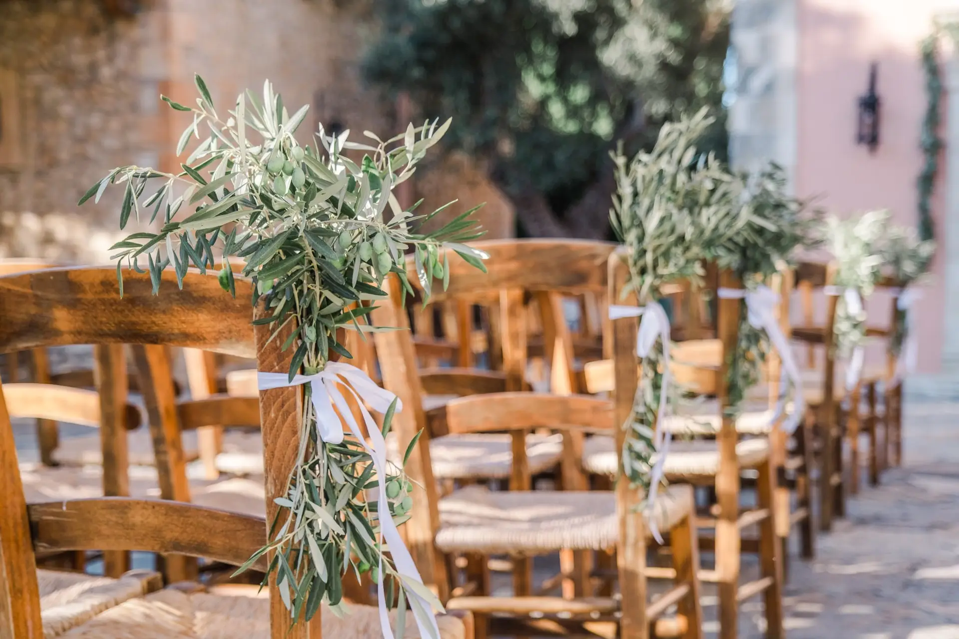 Décoration de cérémonie de mariage à Agreco Farm en Crète, chaises en bois décorées de branches d’olivier photographiées par Julien Boyer photographe de mariage