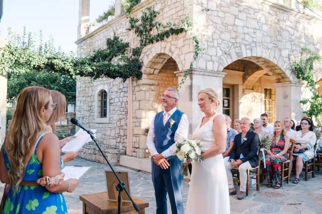 Mariés écoutant l’officiante pendant la cérémonie de mariage à Agreco Farm près de Rethymnon en Crète, moment solennel photographié par Julien Boyer photographe de mariage