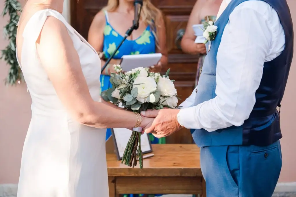 Échange des vœux pendant la cérémonie de mariage à Agreco Farm près de Rethymnon en Crète, mains des mariés et bouquet capturés par Julien Boyer