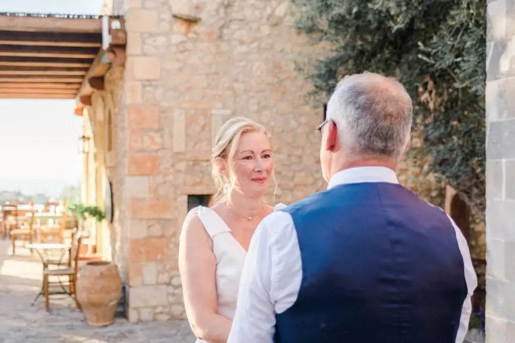 Mariée regardant son époux avec émotion pendant la cérémonie de mariage à Agreco Farm en Crète, lumière naturelle photographiée par Julien Boyer photographe de mariage