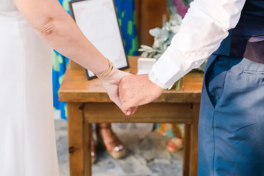 Mains des mariés enlacées pendant la cérémonie de mariage à Agreco Farm près de Rethymnon en Crète, photo naturelle par Julien Boyer photographe de mariage