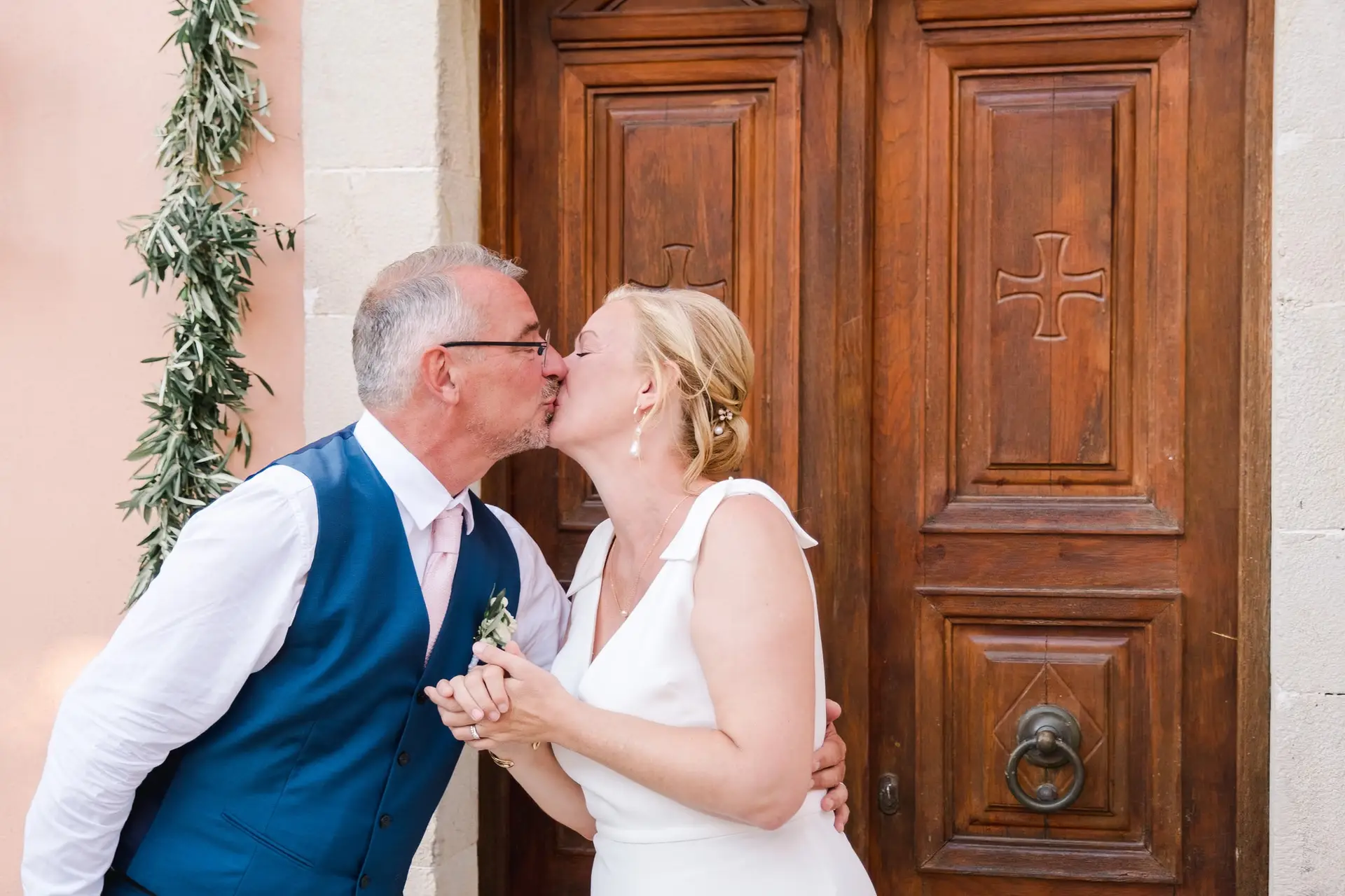 Baiser des mariés devant la chapelle à Agreco Farm près de Rethymnon en Crète, moment romantique photographié par Julien Boyer photographe de mariage