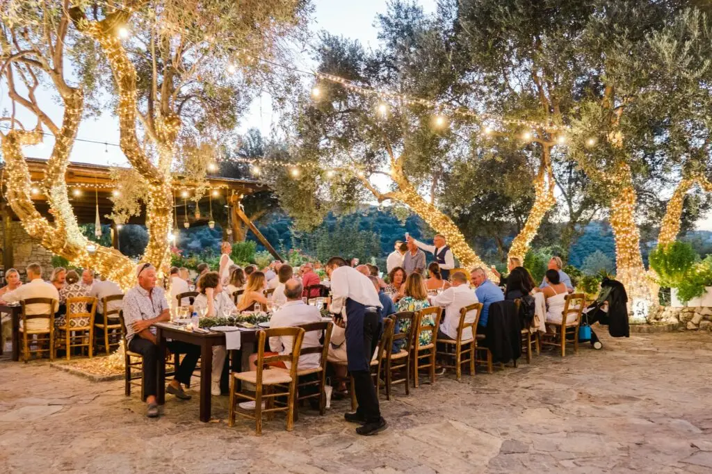 Dîner de mariage en extérieur sous des oliviers illuminés, invités réunis autour de grandes tables en bois à Rethymnon en Crète