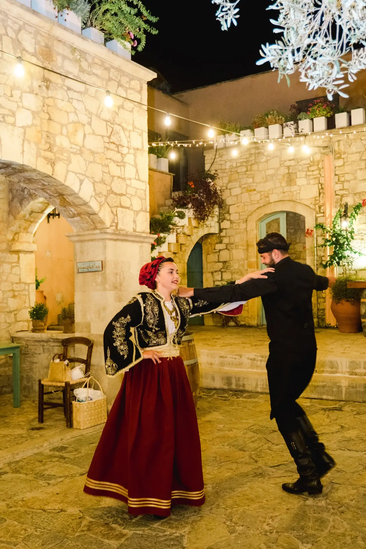 Invités souriants et dansants pendant la soirée de mariage en Crète, décor en pierre, lumières suspendues et ambiance méditerranéenne
