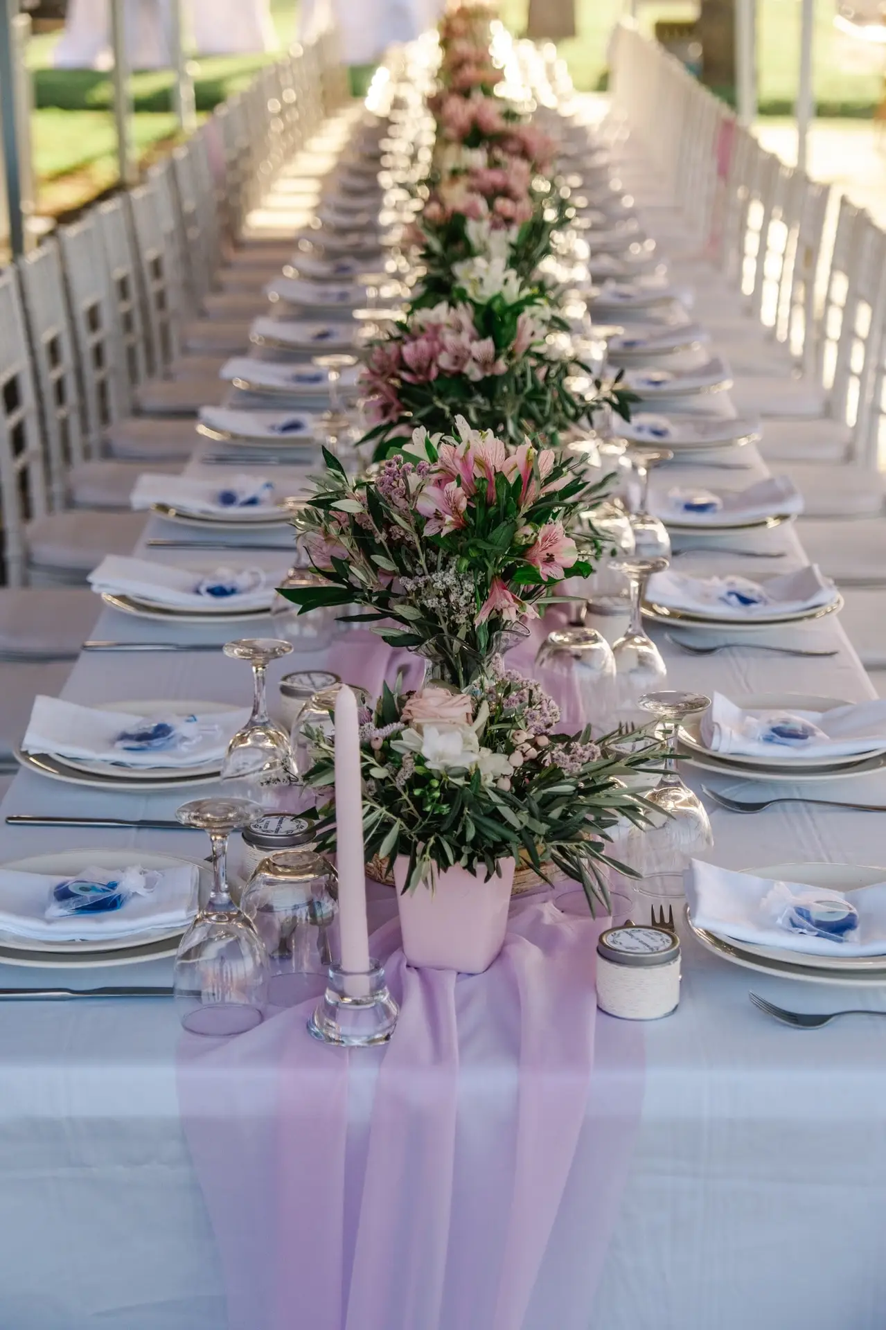 Longue table de réception décorée de compositions florales roses et feuillage méditerranéen lors d’un mariage en extérieur en Crète, photographiée par Julien Boyer photographe de mariage