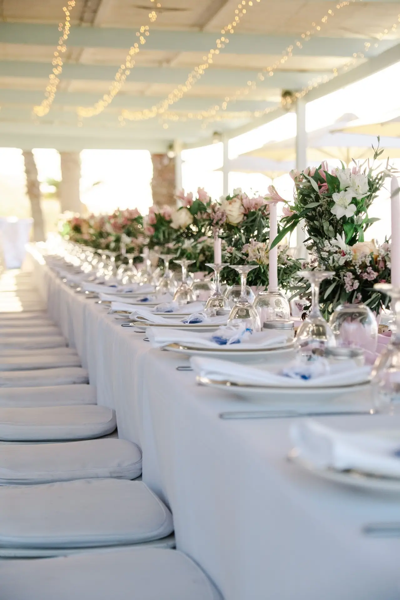 Table de mariage élégante dressée sous une pergola avec guirlandes lumineuses et décor floral pour un mariage en Crète, ambiance douce et raffinée capturée par Julien Boyer
