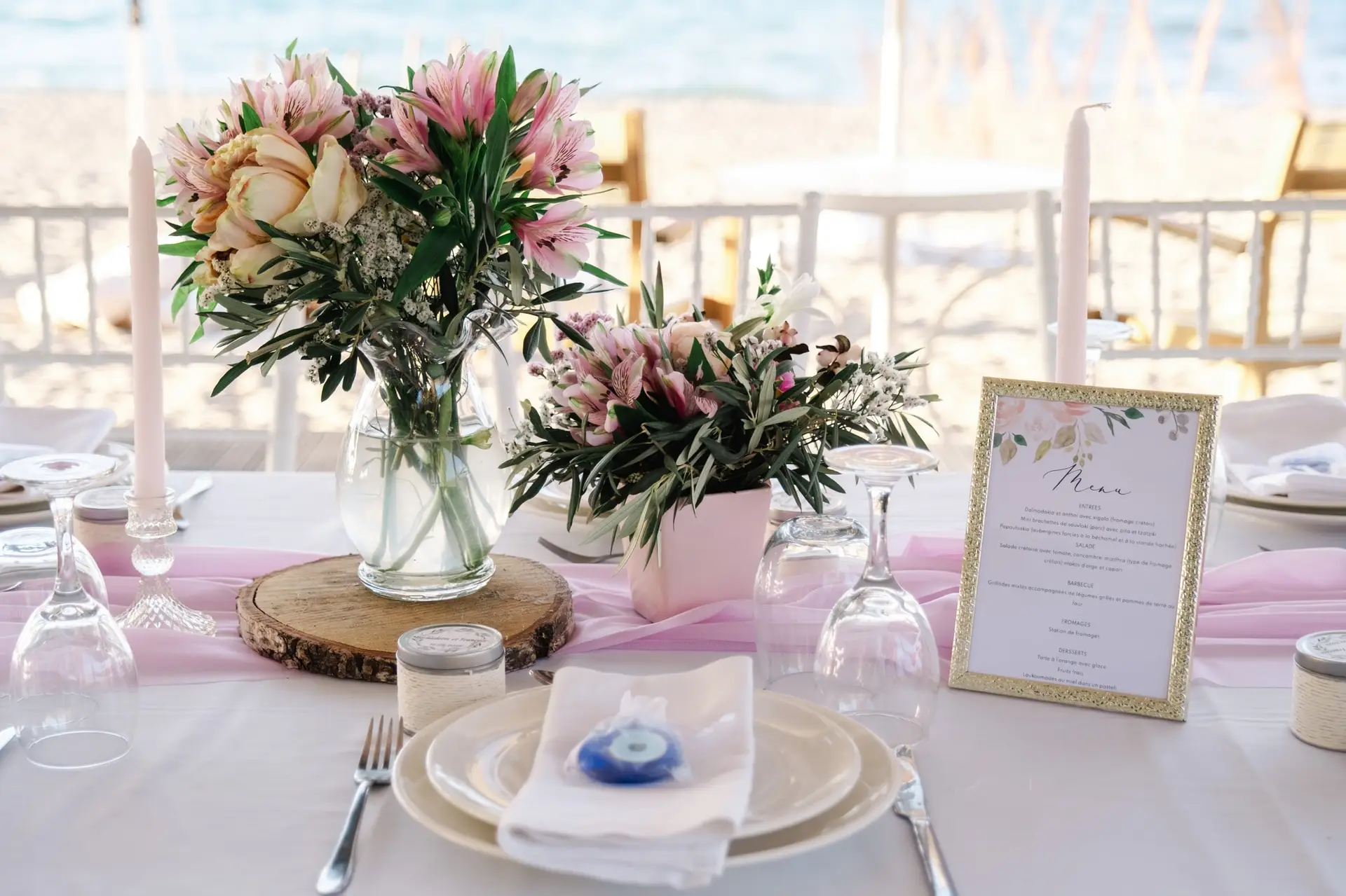 Décoration de table de mariage avec compositions florales roses, bougies et vaisselle élégante face à la mer en Crète, ambiance douce et raffinée