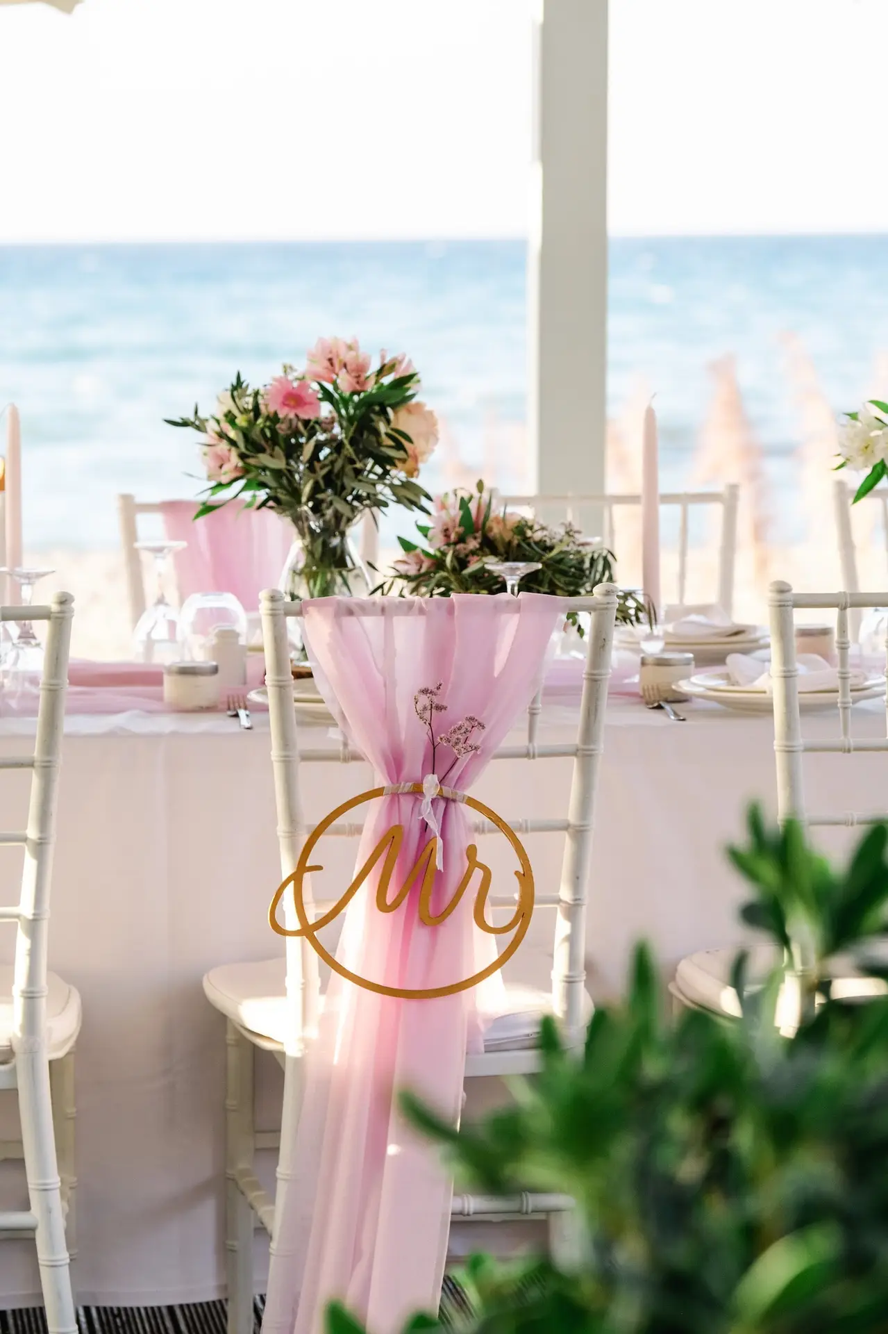 Détail de la chaise du marié décorée de tissu rose et de l’inscription Mr lors d’un mariage en bord de mer en Crète