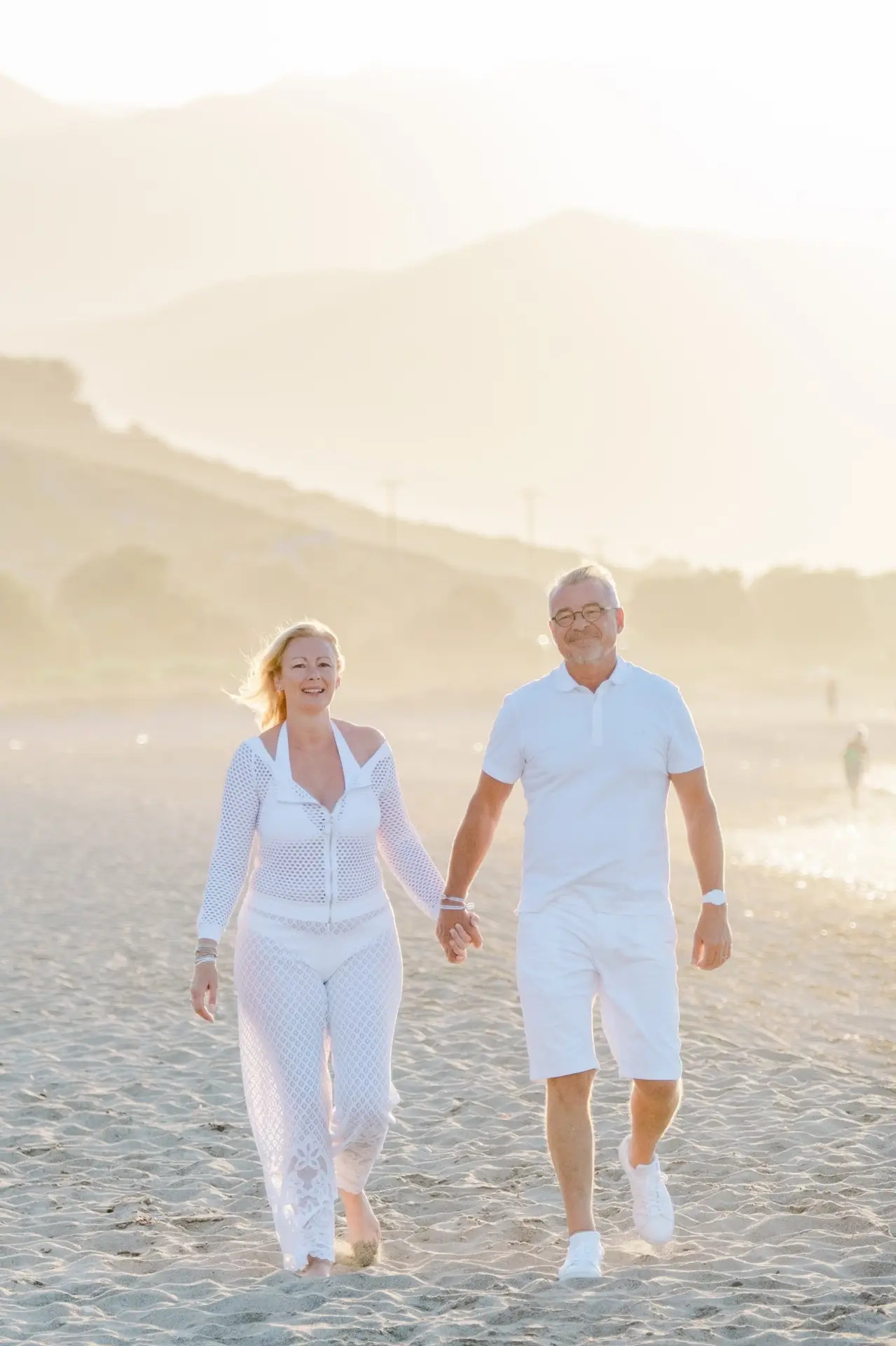 Couple marchant main dans la main sur une plage de Crète à la lumière dorée du coucher du soleil, moment intime et naturel