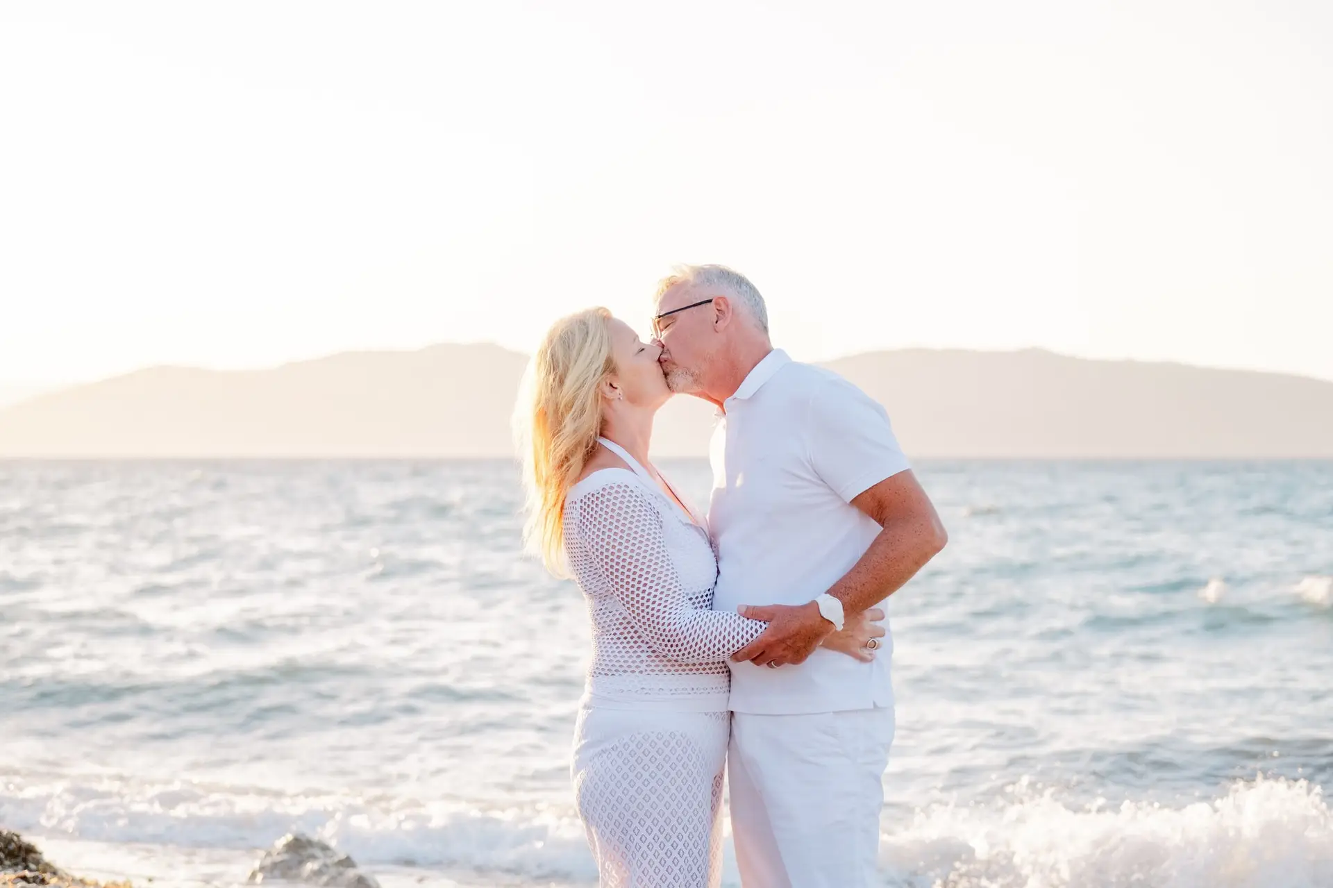 Couple s’embrassant face à la mer en Crète au coucher du soleil, moment romantique sur la plage lors d’un mariage destination