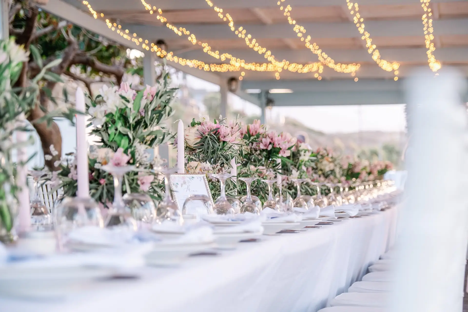 Longue table de mariage décorée de fleurs et guirlandes lumineuses sous une pergola en Crète, ambiance élégante et chaleureuse