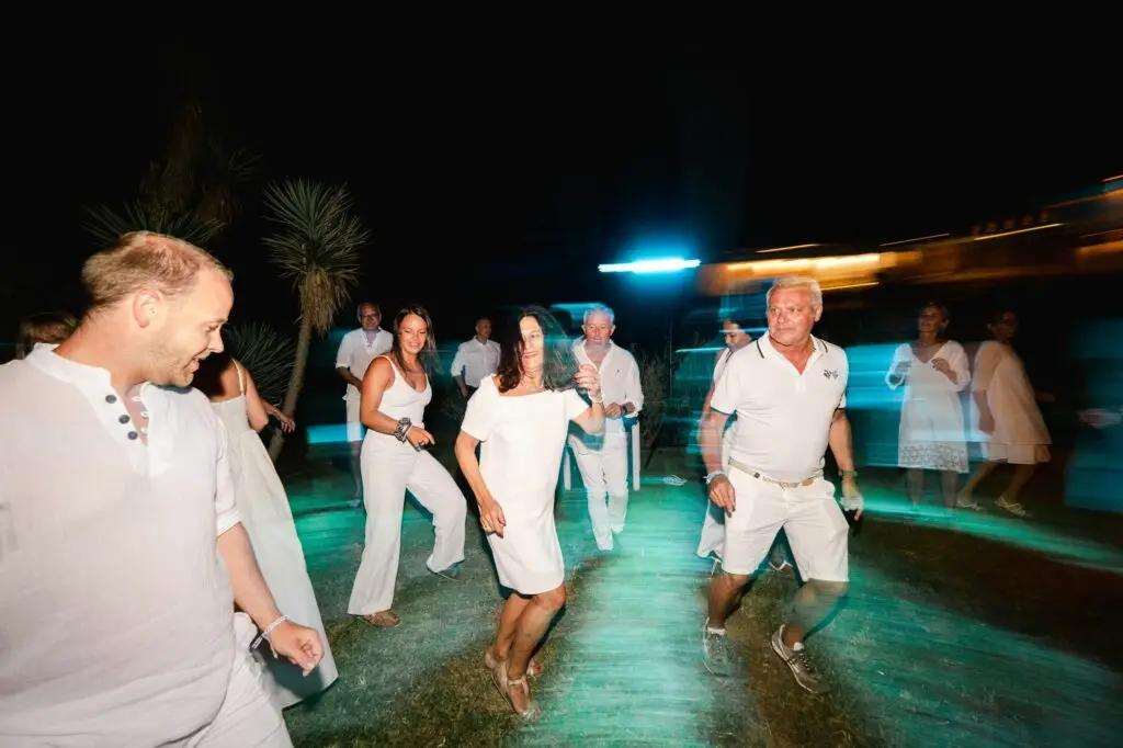 Invités dansant en cercle lors d’un mariage en Crète, atmosphère joyeuse et chaleureuse en extérieur de nuit
