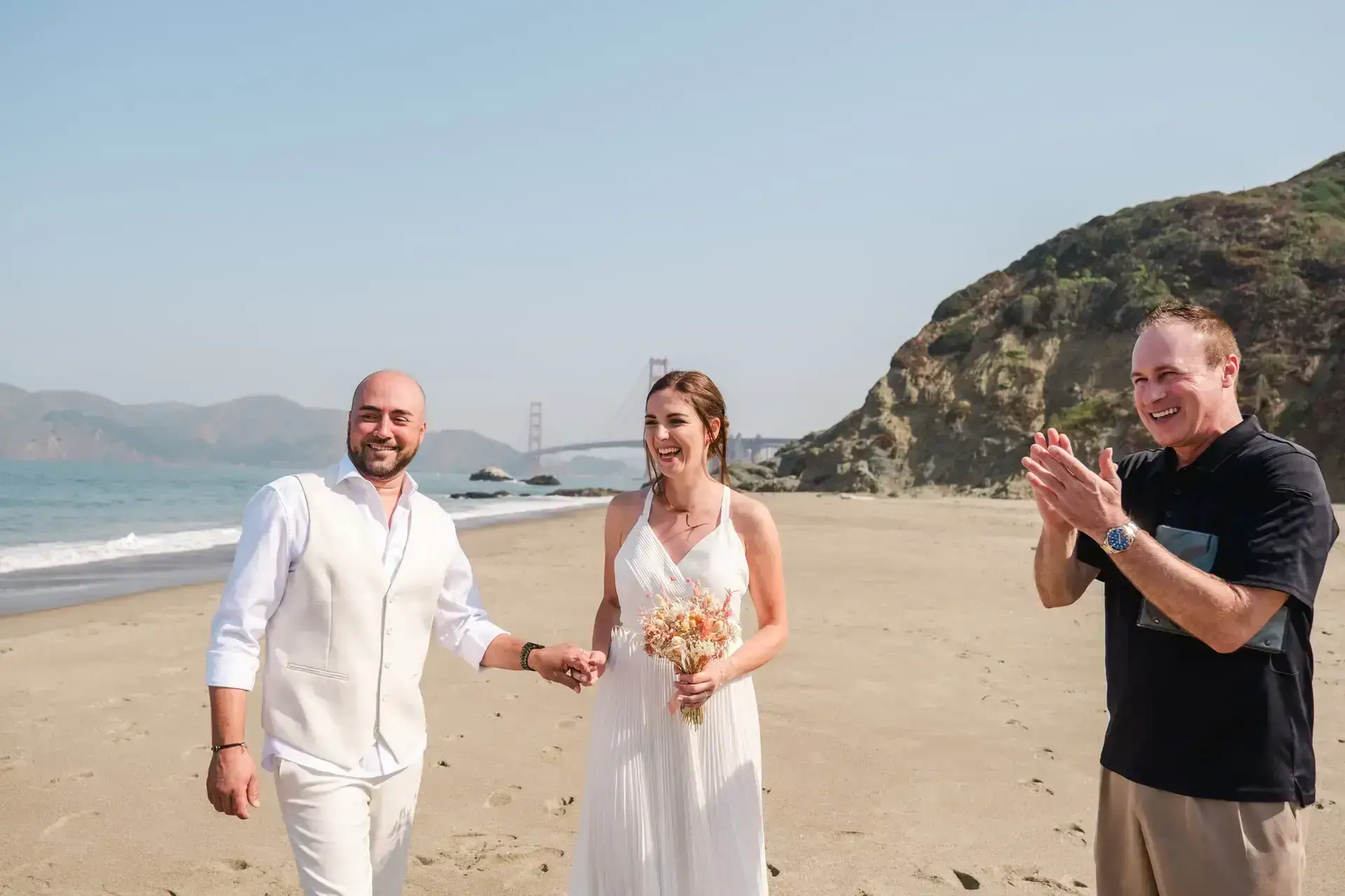 Mariés sortant de leur cérémonie elopement sur la plage à San Francisco avec le Golden Gate Bridge en arrière-plan photographié par Julien Boyer