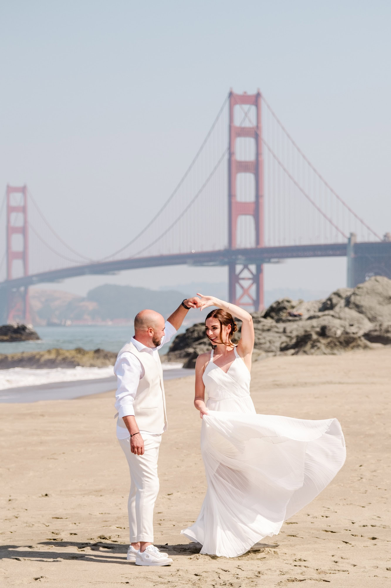 Mariés dansant sur la plage pendant leur elopement à San Francisco avec le Golden Gate Bridge
